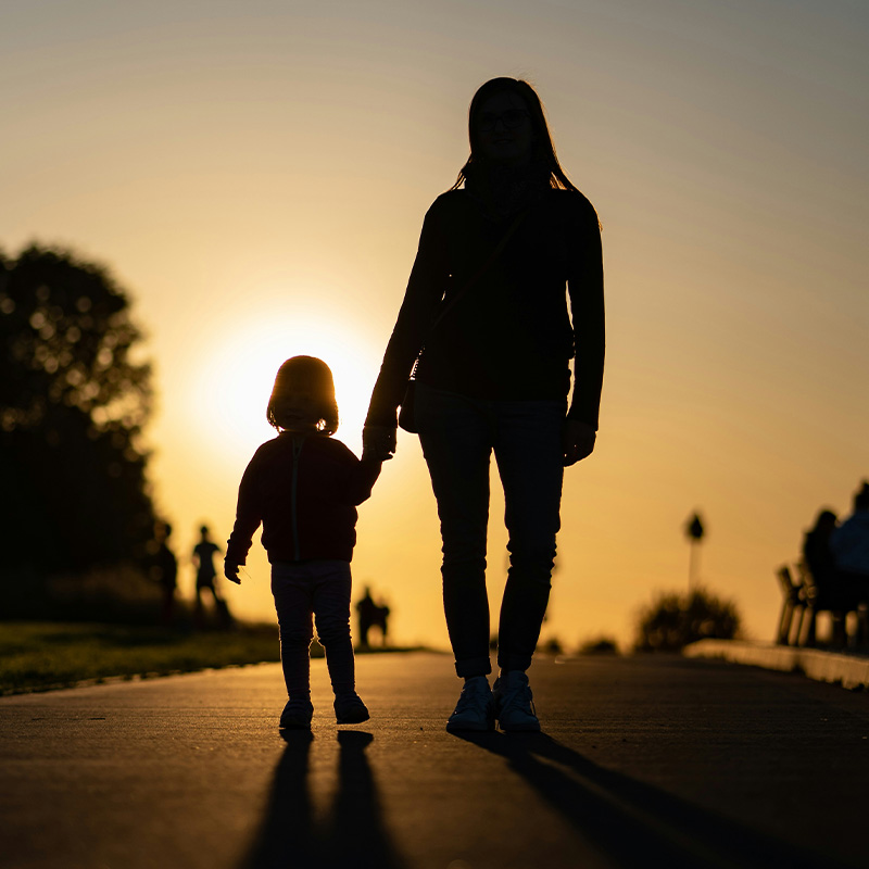 Silhouette of a mother and daughter walking towards a glowing sunset.