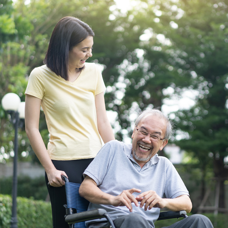A daughter pushing her father in a wheelchair while they smile and laugh.