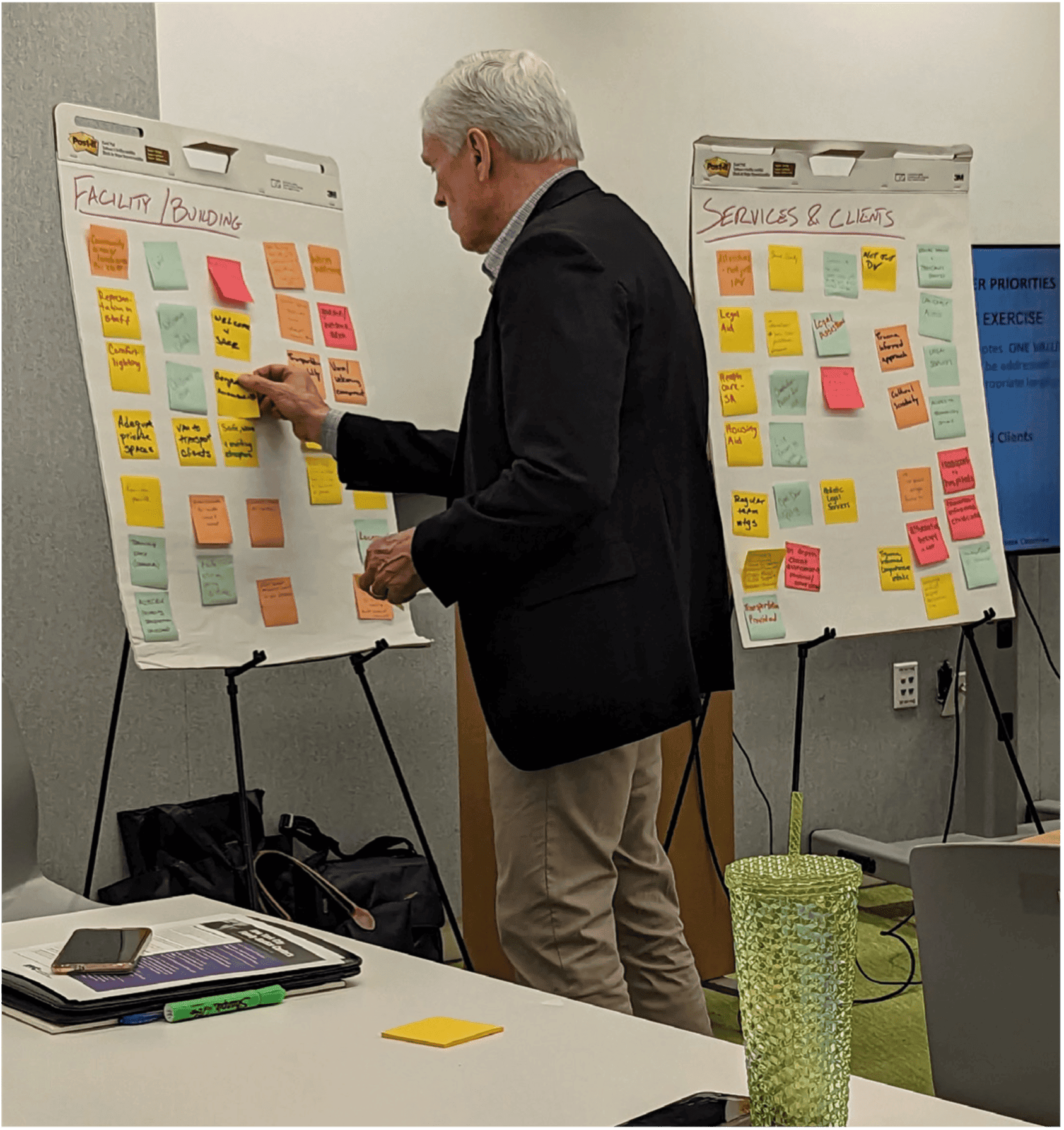 An older man walking over to a board and placing a post-it note on a board of others post-it notes.